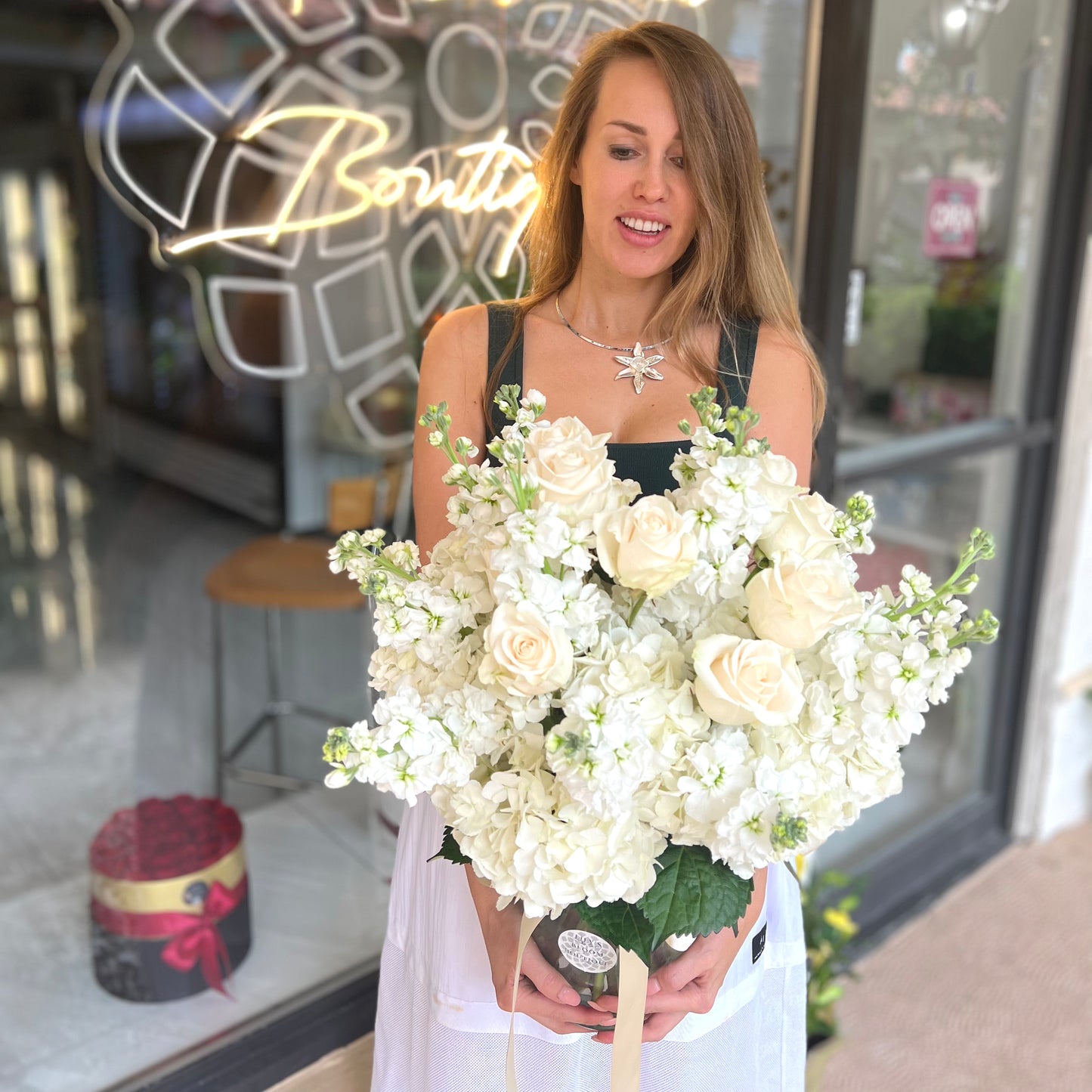 A woman holding beautiful white flowers vase in front of Lily's Bloom Boutique store
