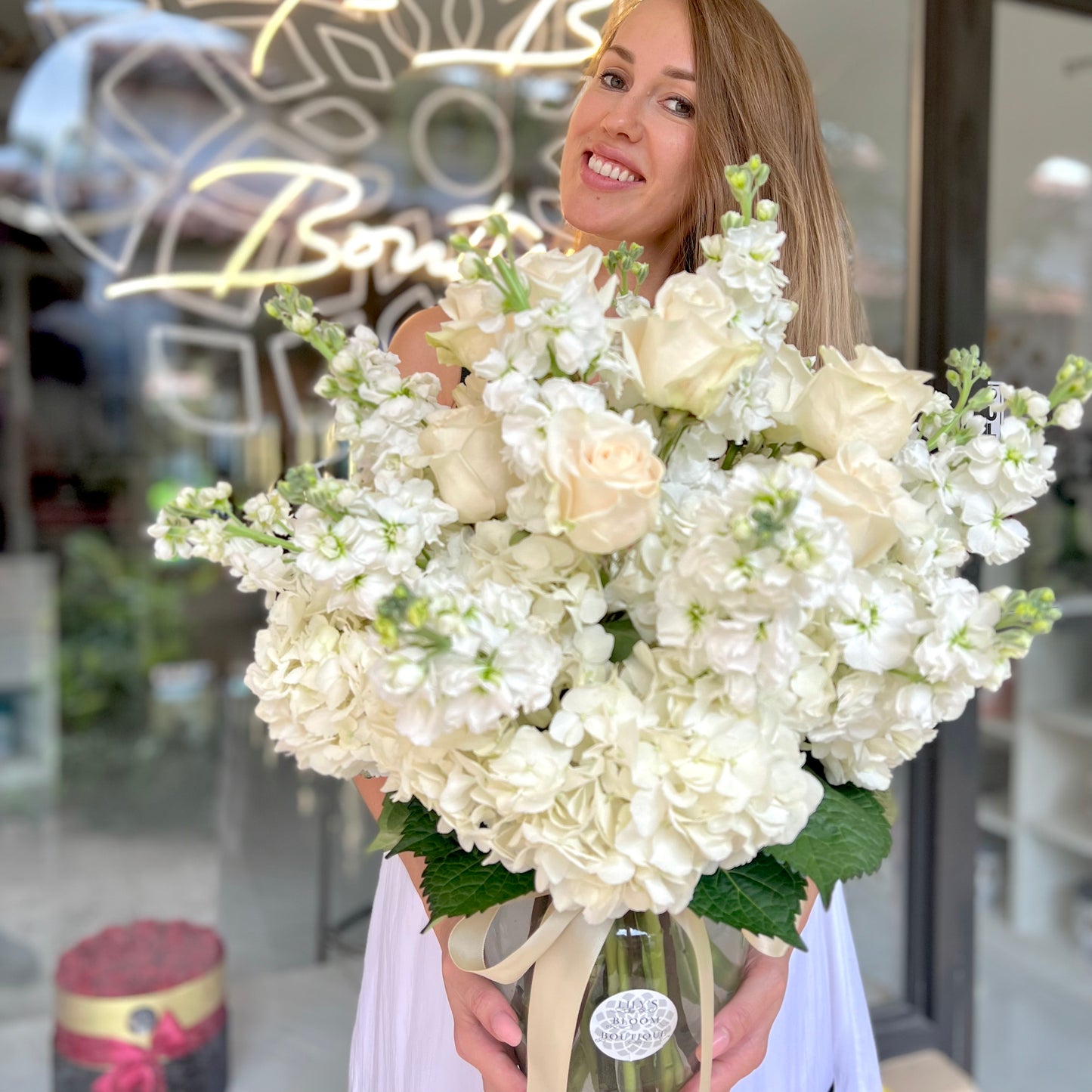 A beautiful woman with long brown hair holding adorable white flowers in clear vase