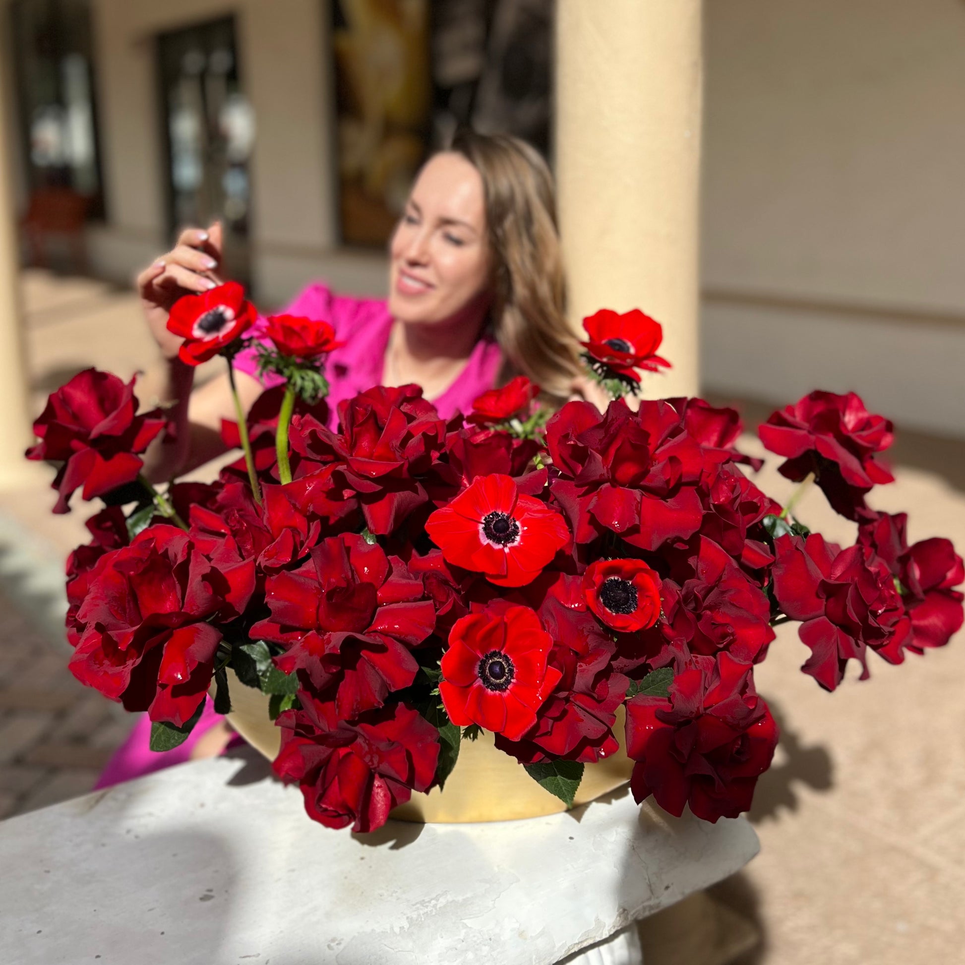 Red roses and red anemones in a gold vase placed on the ground with a lady behind