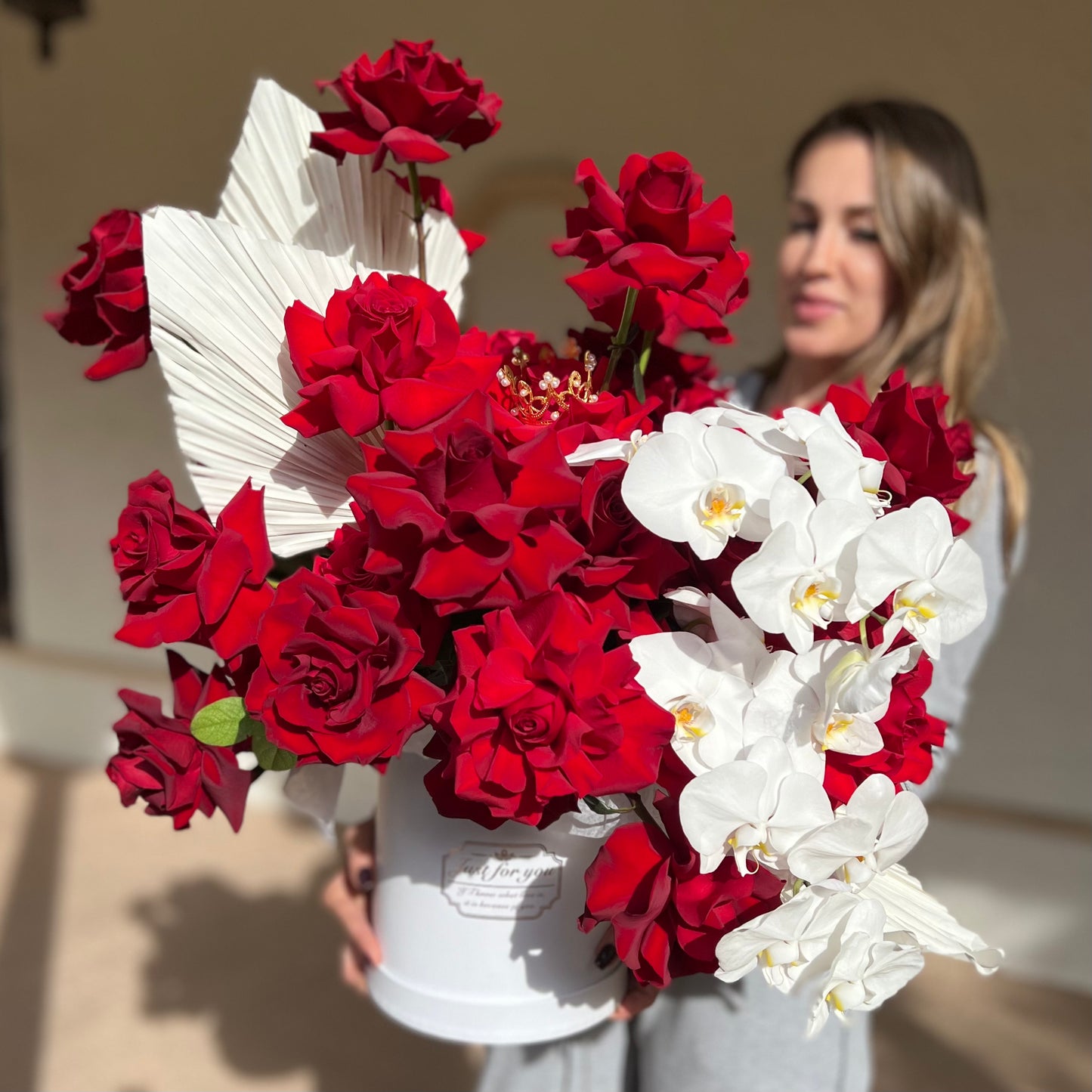 Red roses and white orchids with a crown on top in a white round box