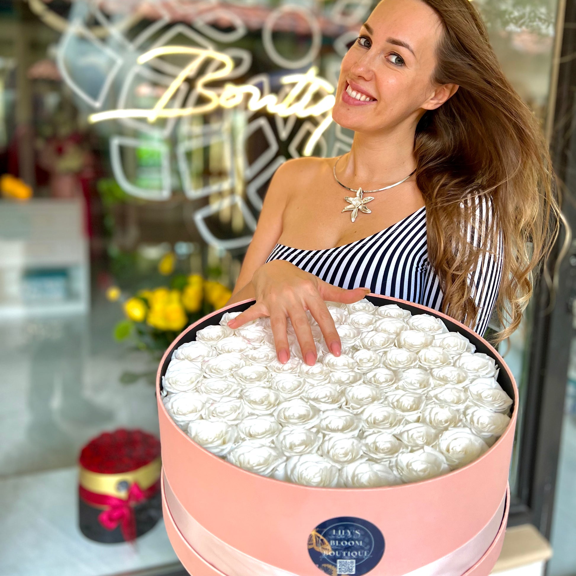 A beautiful smiling woman holds large pink box of white roses