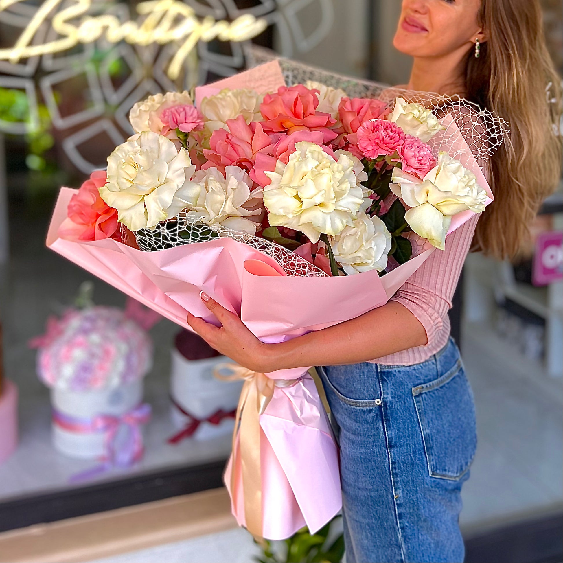 Women in blue jeans holding colorful flower bouquet in pink tissue paper 