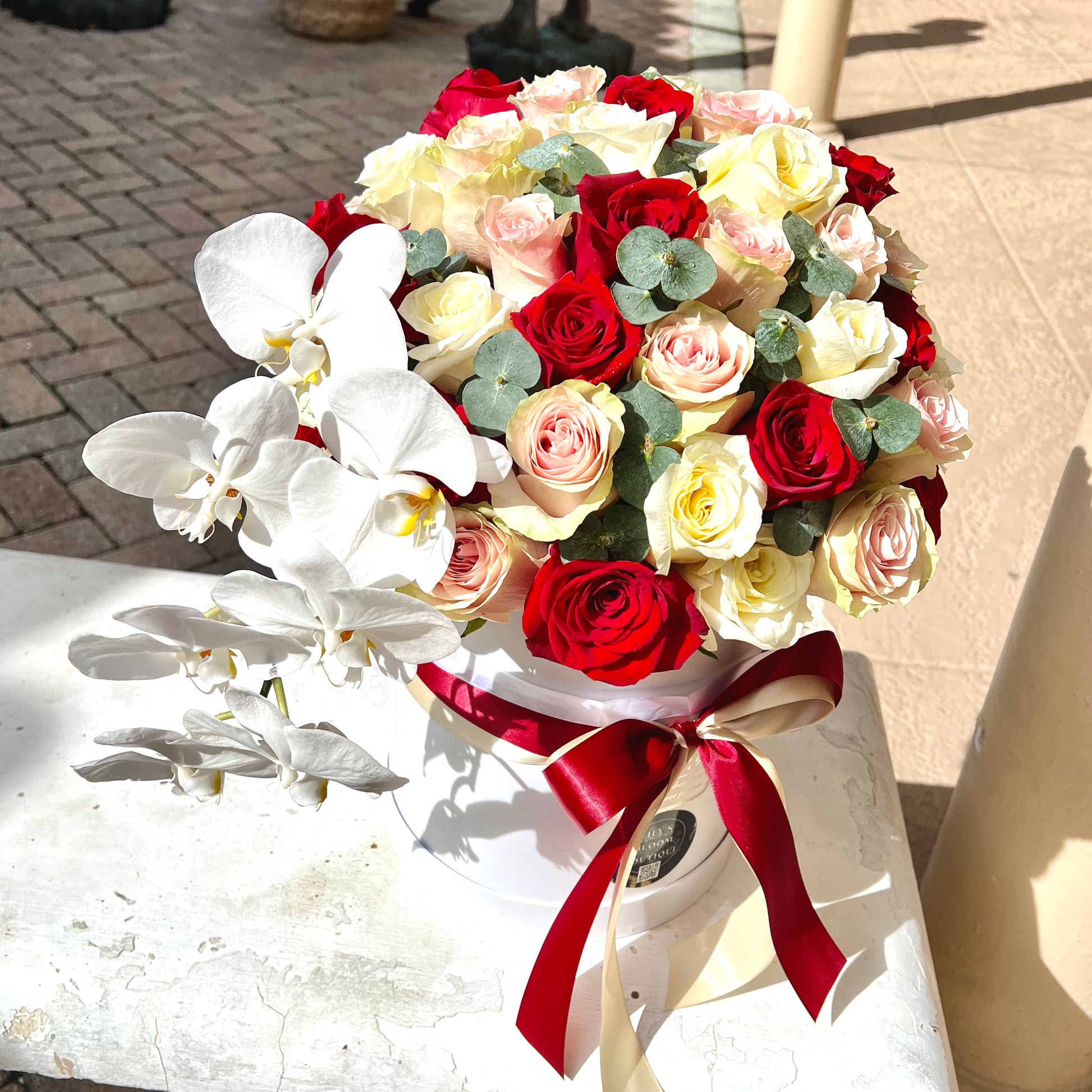 Red, yellow roses in white round box with sun on them with red ribbon