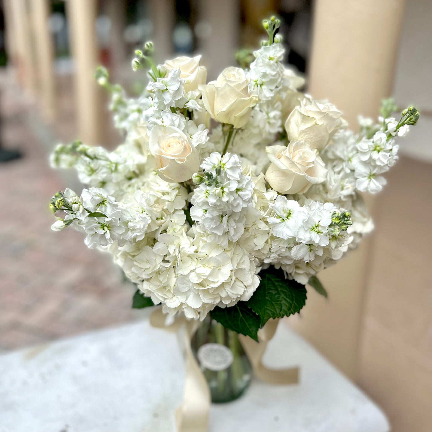 White roses, white stock flowers and hydrangeas in clear vase on concrete bench