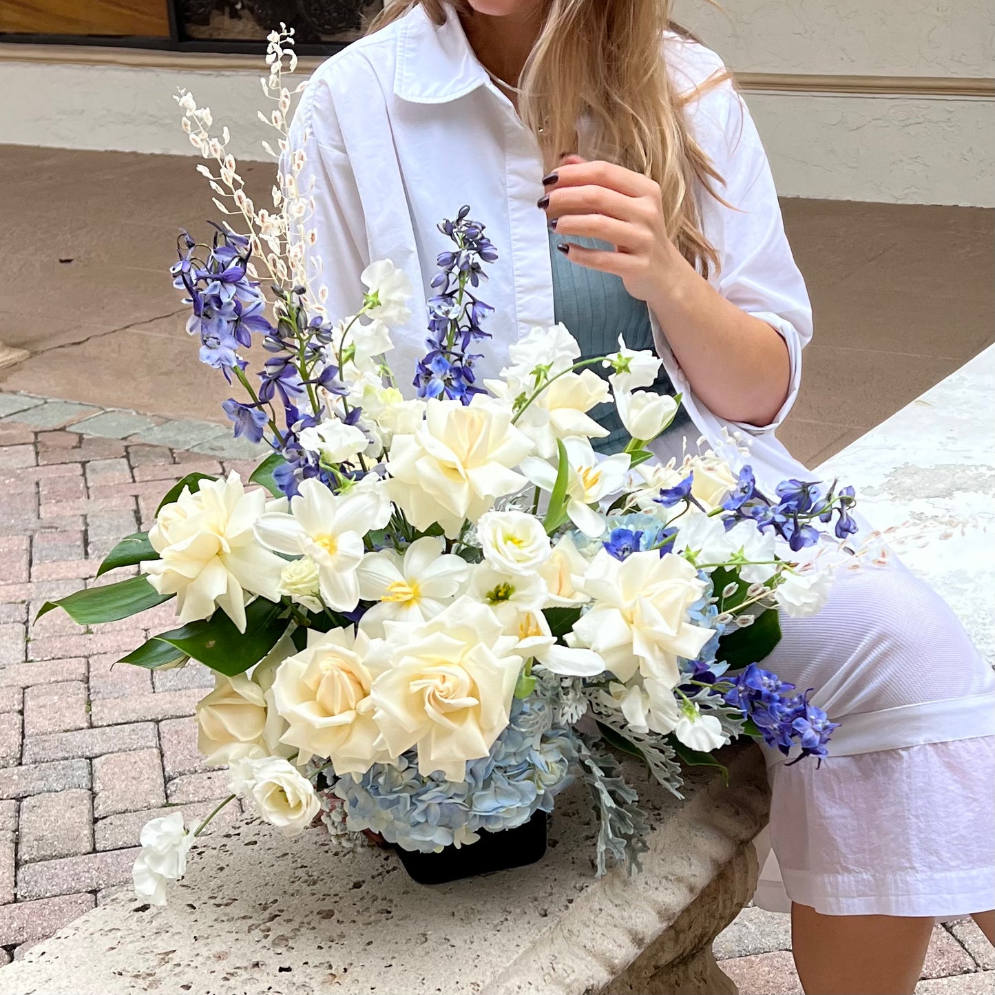 A vase with premium white roses, tulips, lisianthuses, blue hydrangeas, delphinium and Dusty Miller