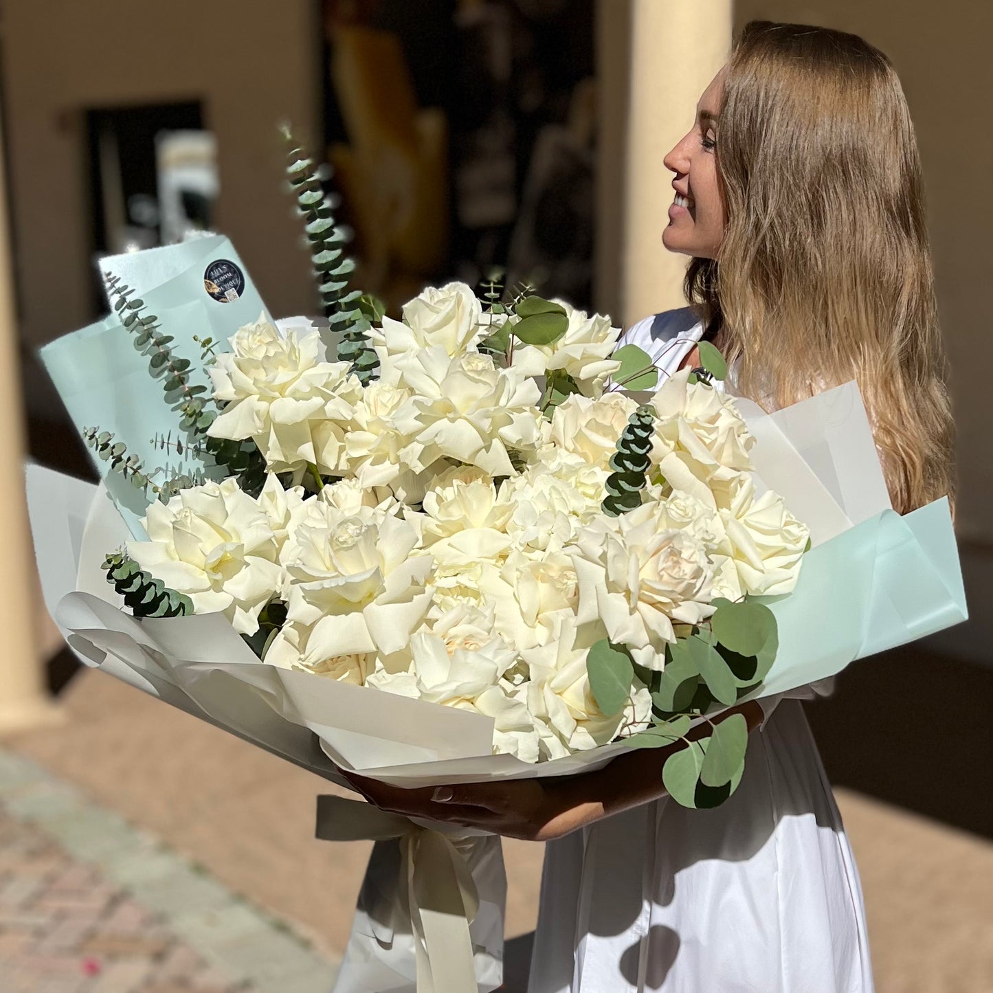 A woman carrying a large white bouquet of premium roses