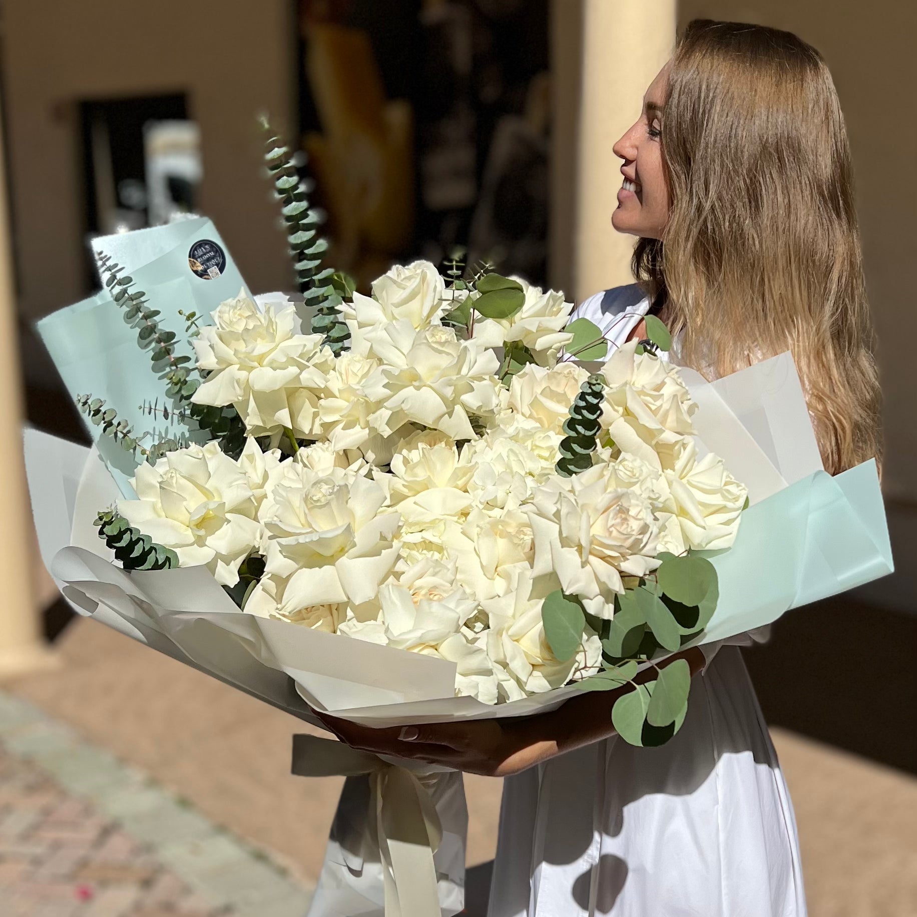 A woman carrying a large white bouquet of premium roses