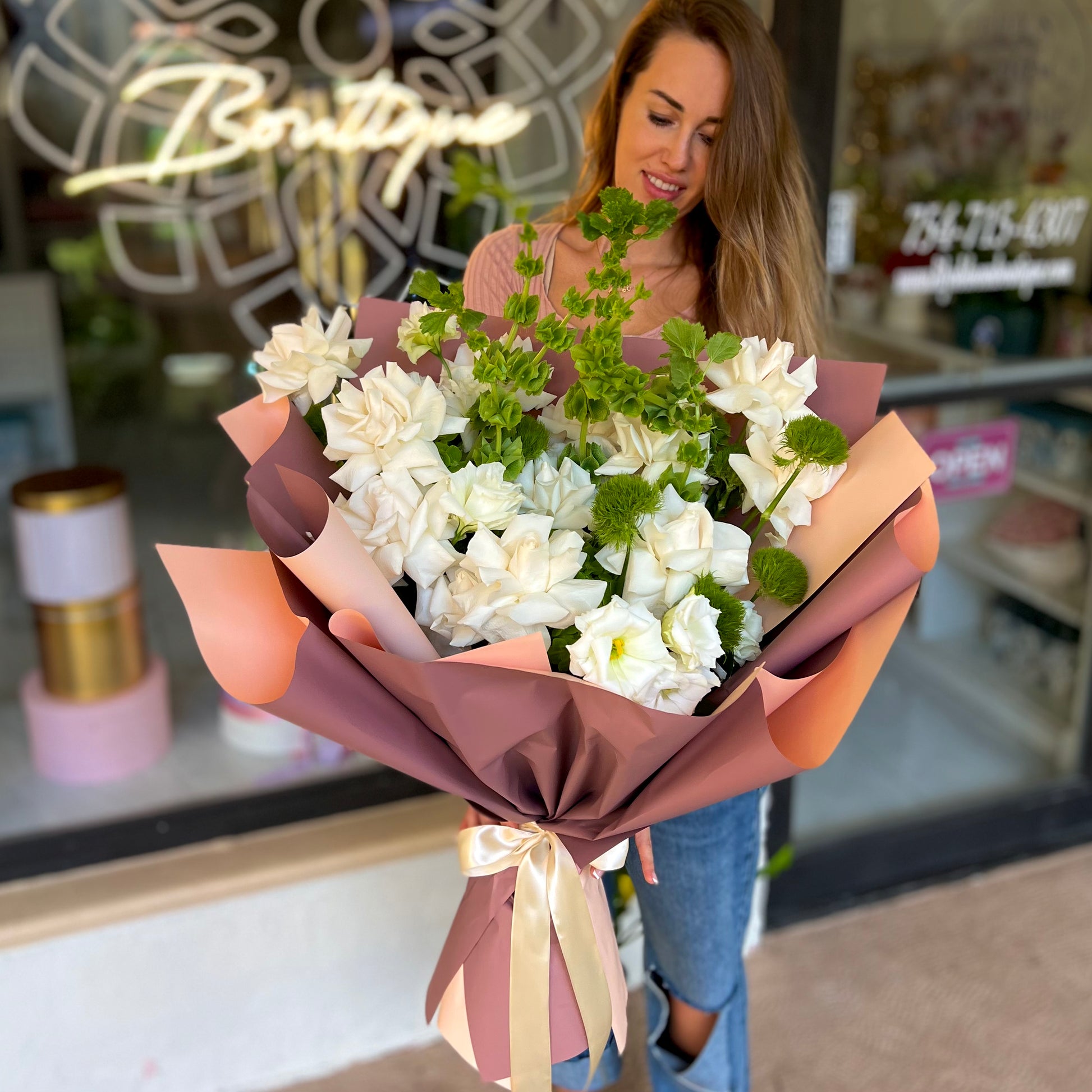 Women with long brown hair holding white flowers outside store front 