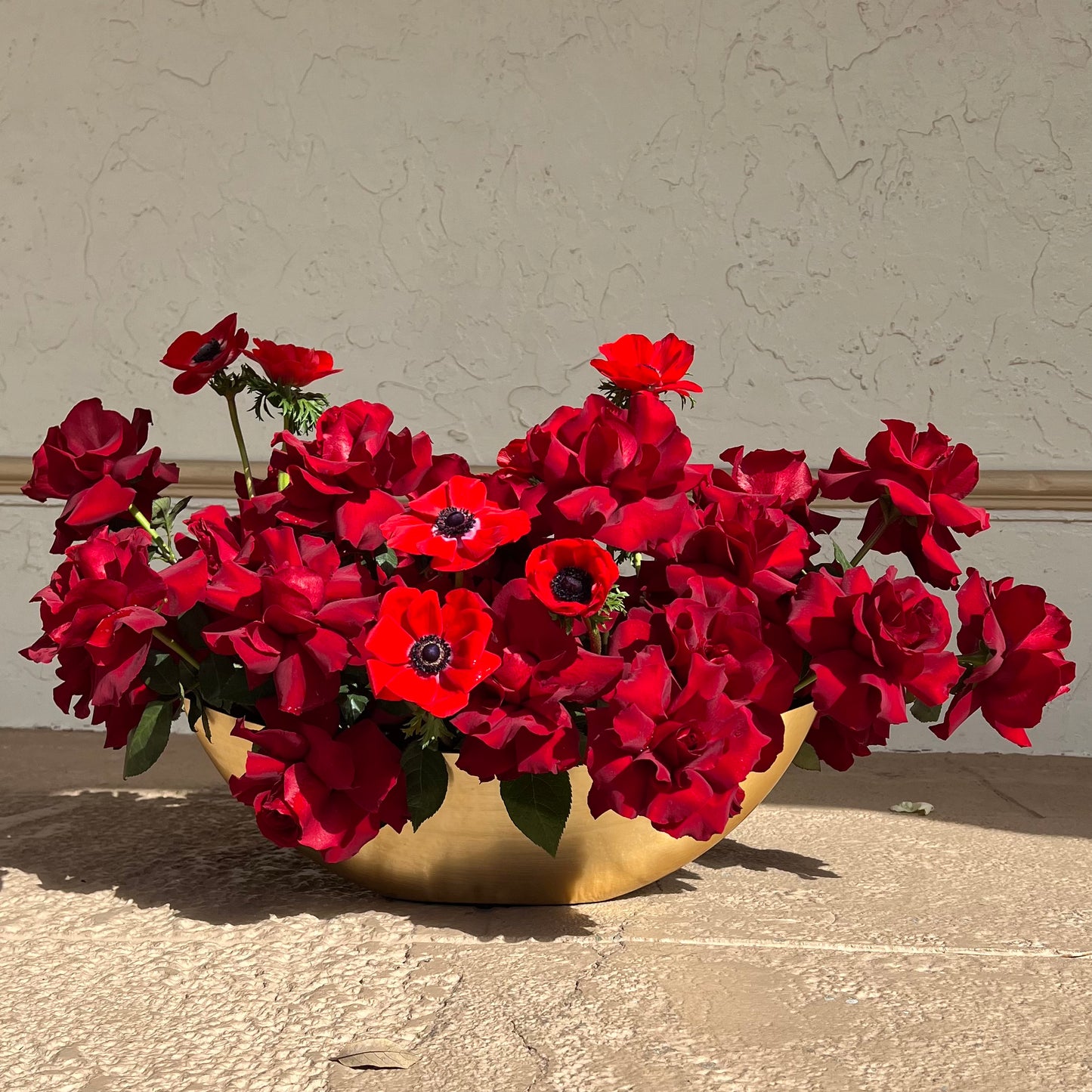 Red roses and red anemones in a gold vase placed on the ground